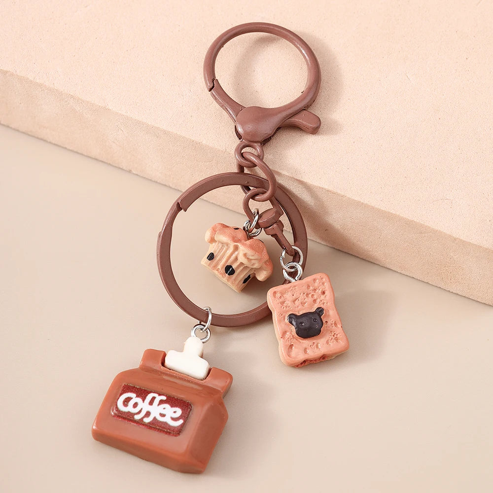 A brown clay coffee-themed keychain featuring a coffee jar and a cat charm on a leather loop.