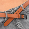 A close-up of a tan leather belt with a black buckle laid across a gray denim jean pocket.