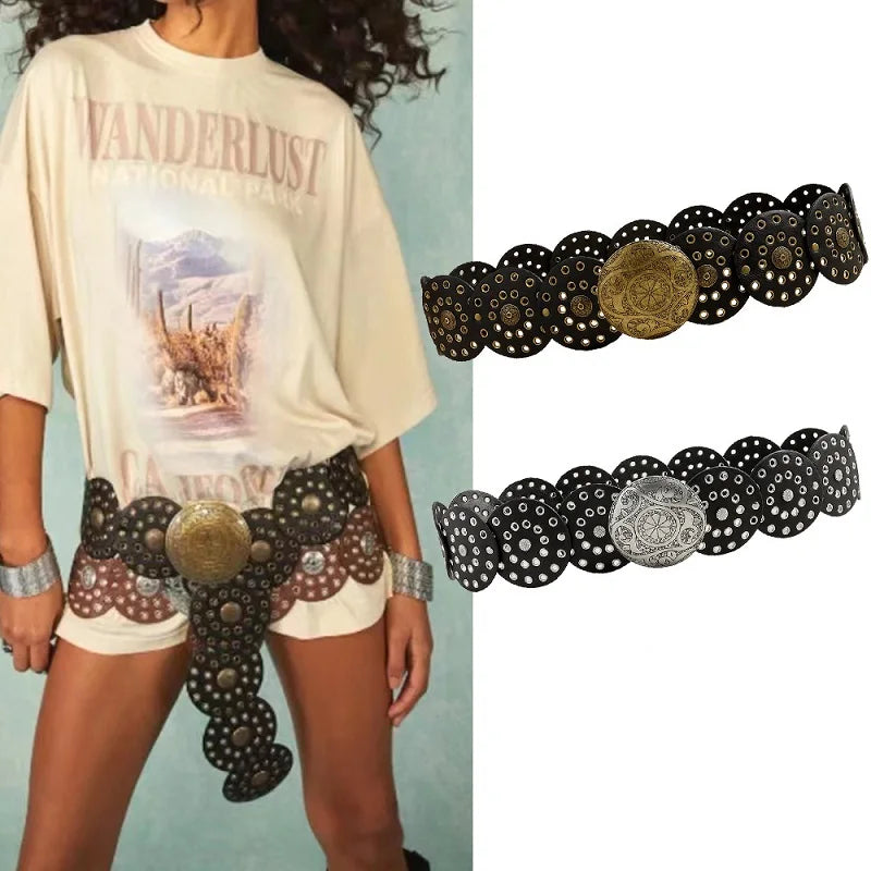 A woman wearing a light-colored t-shirt and denim shorts displays a vintage western belt with gold and black decorative studs