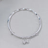 A silver sterling silver bell bangle bracelet worn on a light gray surface.