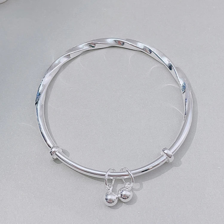 A silver sterling silver bell bangle bracelet worn on a light gray surface.