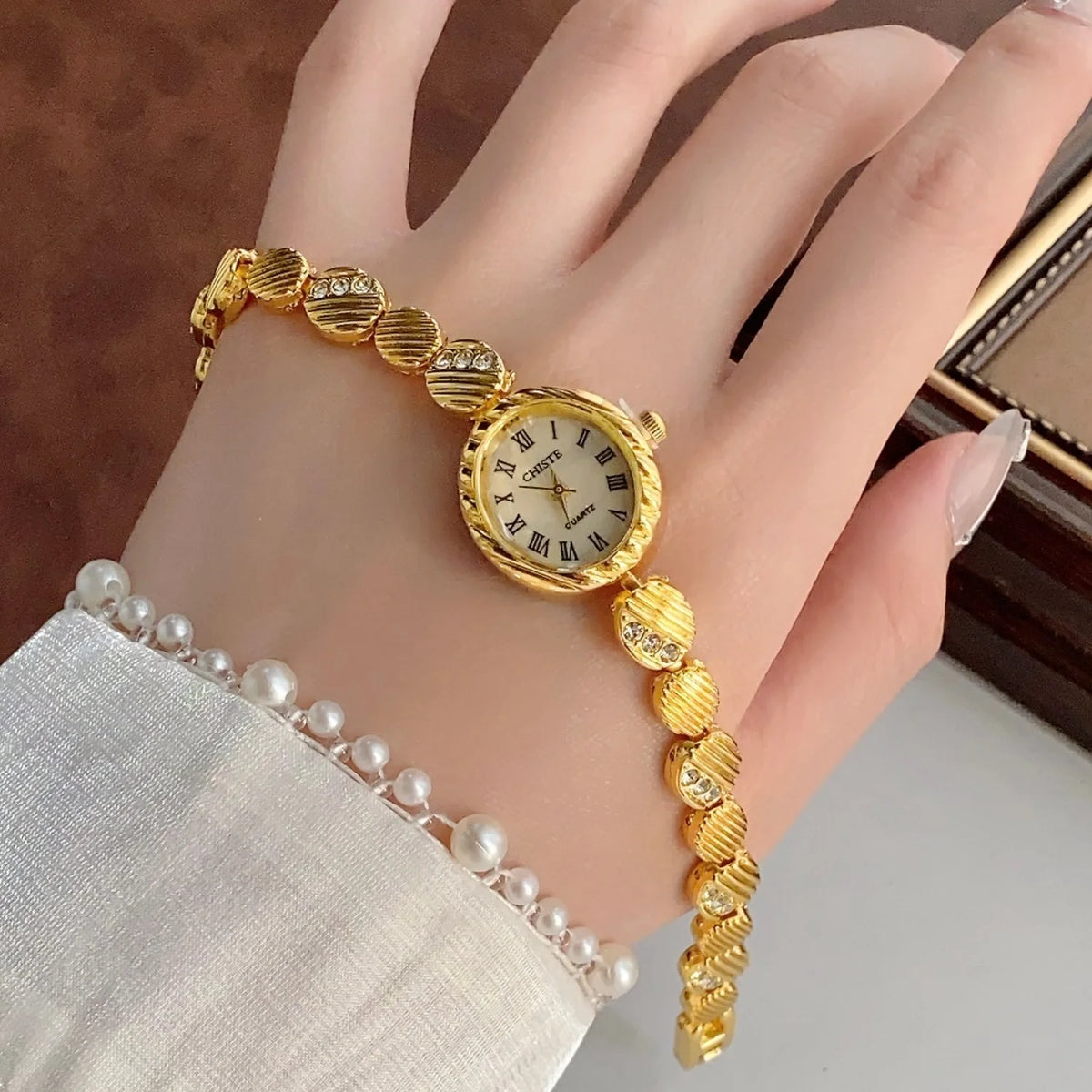 A gold quartz fashion wristwatch with a beaded bracelet worn on a hand against a dark background.