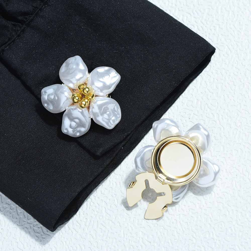 Silver and white baroque pearl button covers with gold accents displayed on a black fabric.