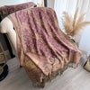 A purple and gold bohemian paisley tassel shawl draped over a light-colored chair.