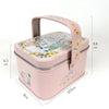 A pink decorative tinplate candy box with a carrying loop and floral design.