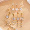 A set of gold heart and flower dangle curved belly piercing jewelry featuring various diamond and pearl accents.