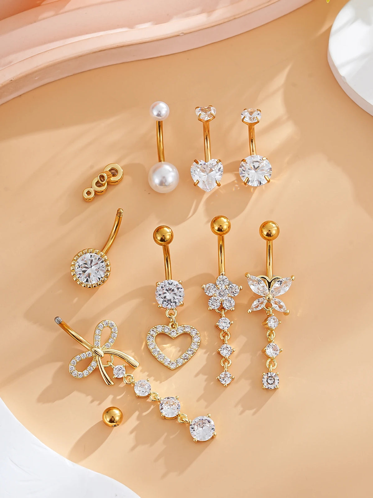 A set of gold heart and flower dangle curved belly piercing jewelry featuring various diamond and pearl accents.