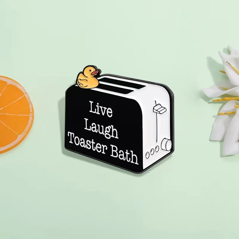 A black enamel pin shaped like a loaf of bread with a duck sitting on top.