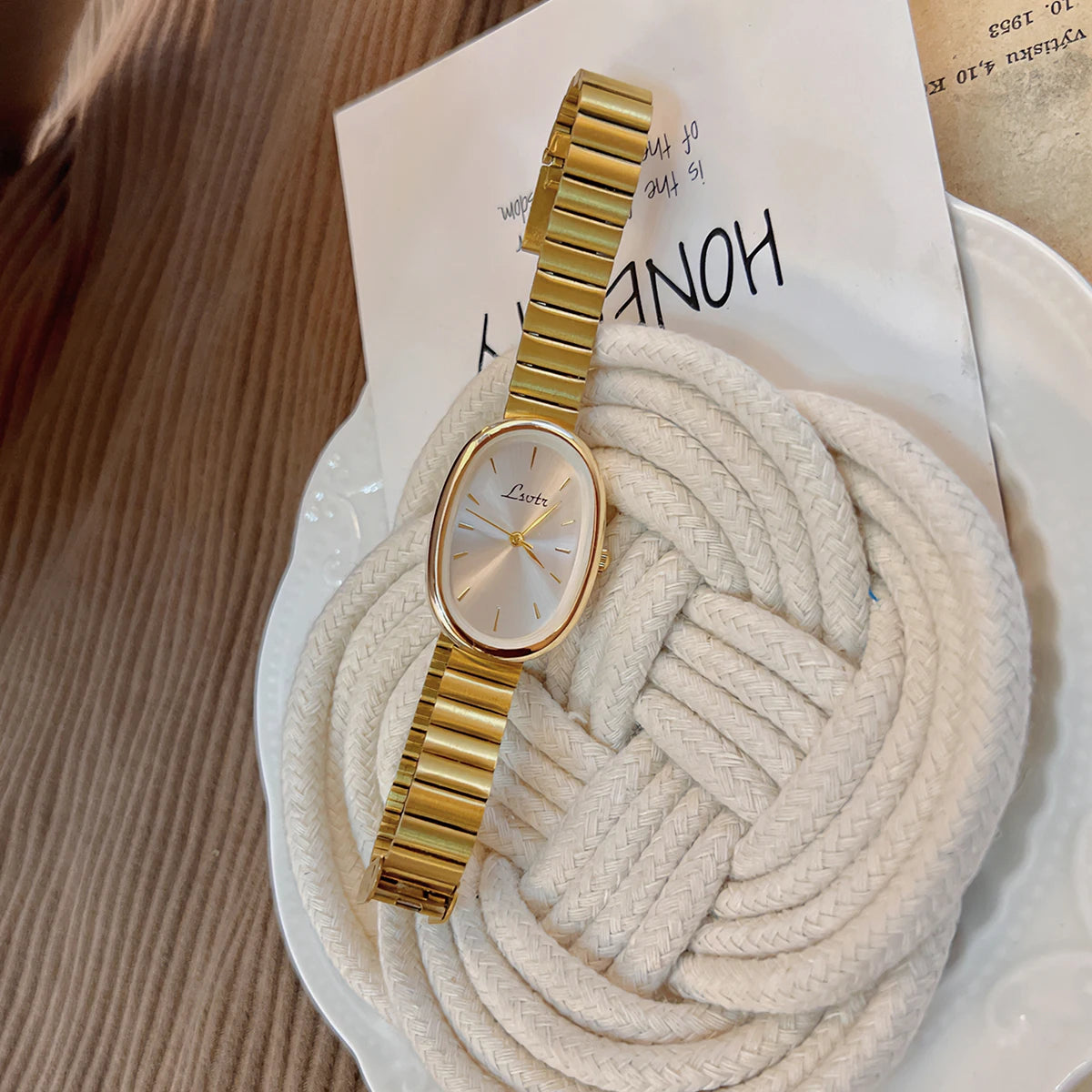 Montre en quartz doré avec cadran clair, présentée sur fond blanc à côté d'une corde épaisse de couleur crème.