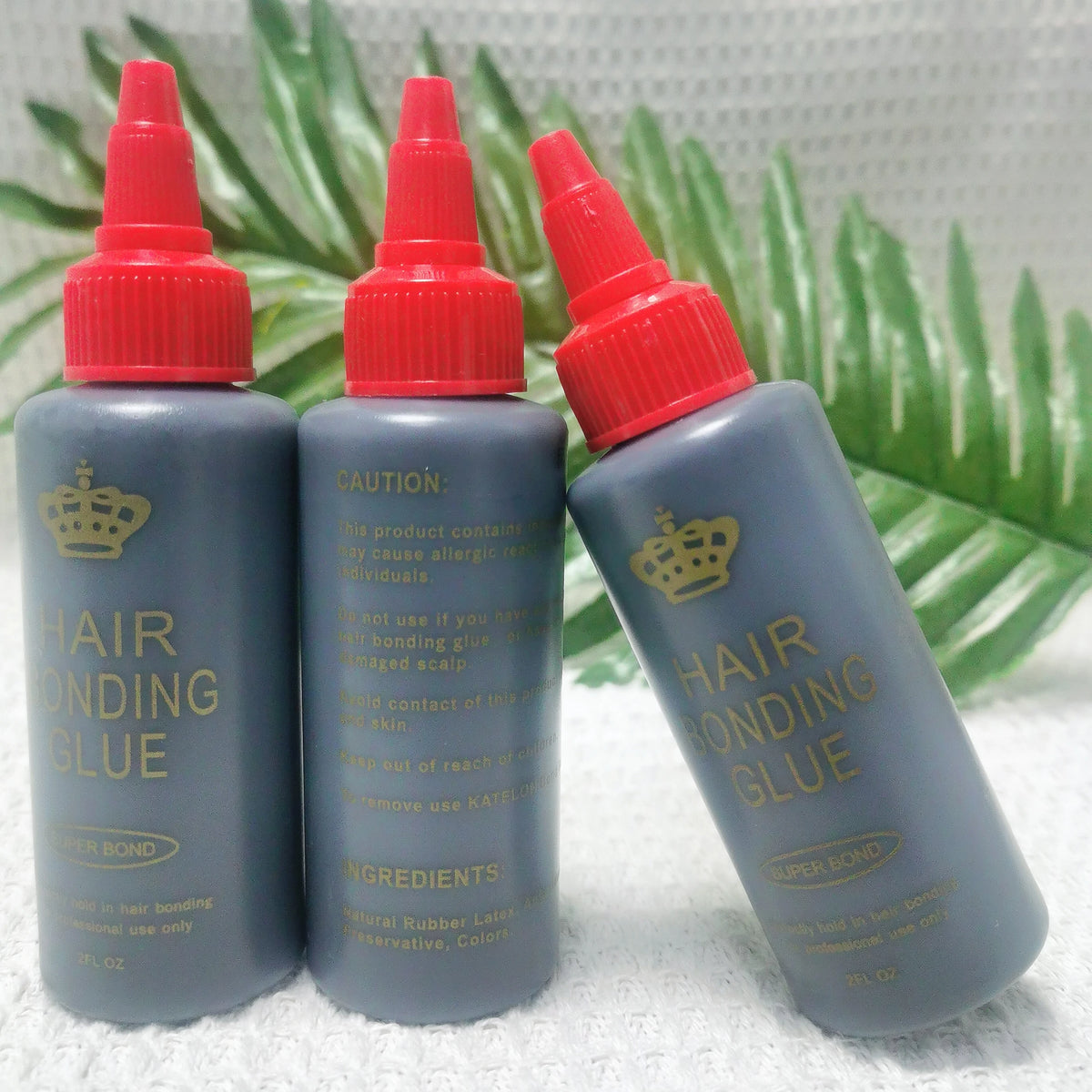Three bottles of professional hair bonding glue in dark gray plastic with red caps set against a green leaf background.