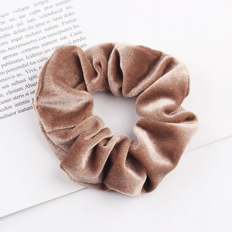 A close-up of a set of six velvet scrunchies in a dusty rose color, folded on a white background.