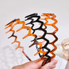 A hand holds a spiral arrangement of textured hair bands in shades of black, orange, and brown.