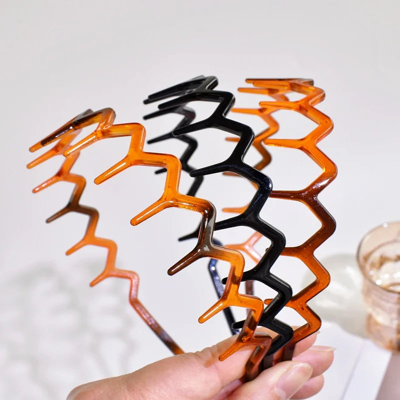 A hand holds a spiral arrangement of textured hair bands in shades of black, orange, and brown.
