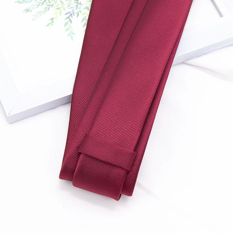 A close-up of a maroon men's slim jacquard business tie lying on a white surface.