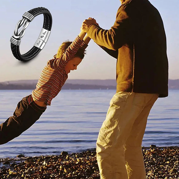 A person is helping a child tie a personalized leather knot bracelet outdoors near the water.
