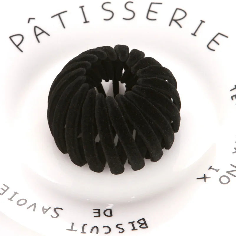 A black, coiled hair clip resembling an horsetail is shown on a white background.