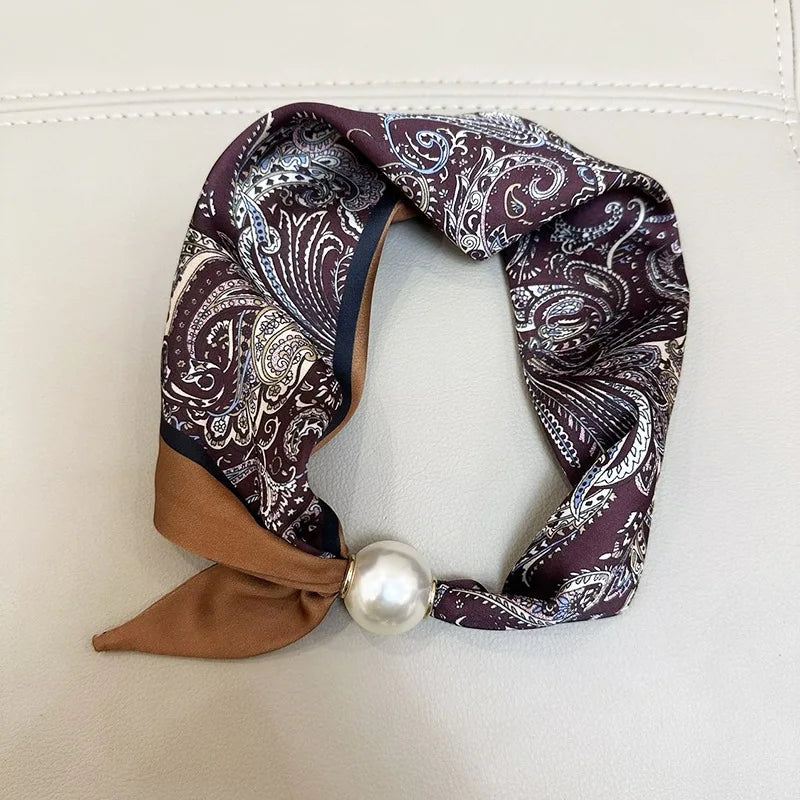 A purple and white paisley scarf tied with a tan fabric and finished with a pearl bead.