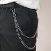 Primer plano de una cadena de cintura de metal plateado, sujetada a un cinturón negro y puesta sobre pantalones oscuros.
