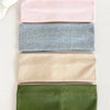 A set of four knitted hair bands in pink, gray, beige, and olive green laid out on a light surface.