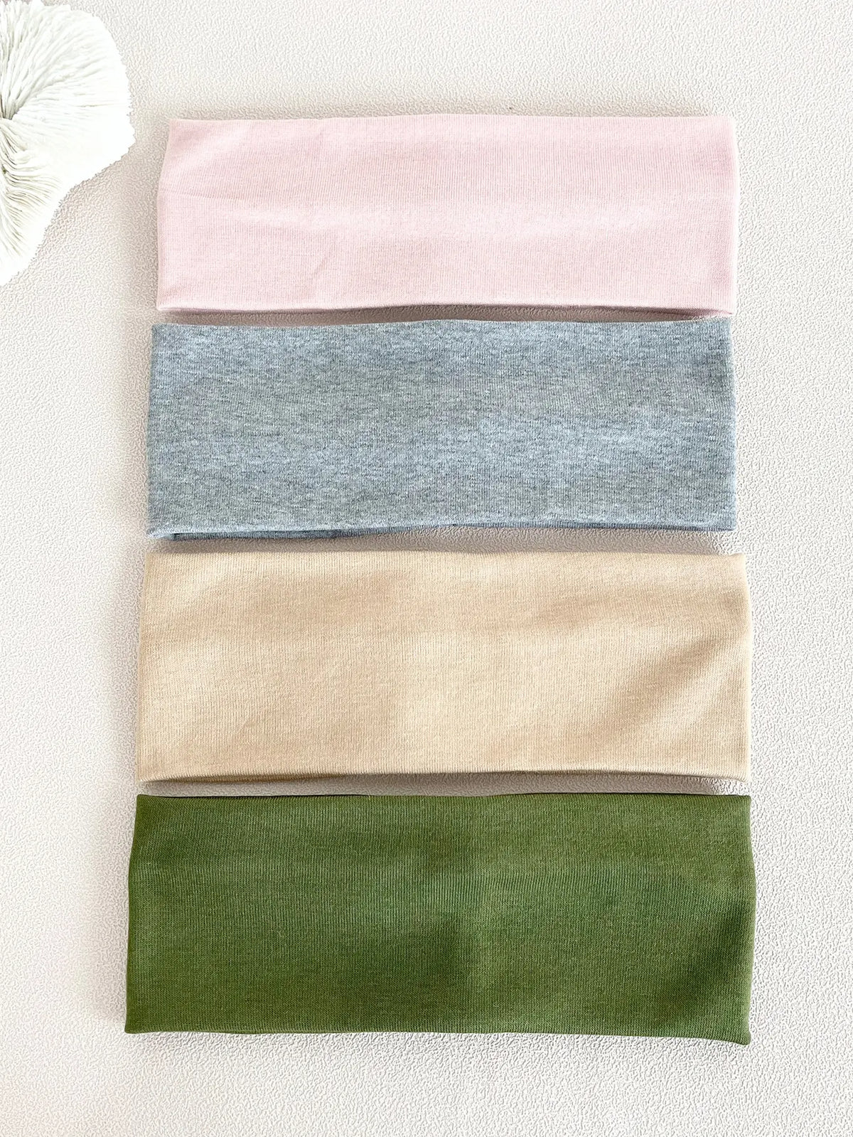 A set of four knitted hair bands in pink, gray, beige, and olive green laid out on a light surface.