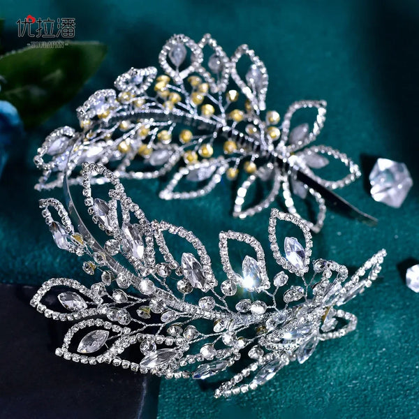 A delicate silver rhinestone leaf bridal hairband with small gold accents, displayed against a dark teal background.