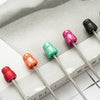 A collection of beadable ballpoint pens in various colors, including red, pink, and green, resting on a light surface.