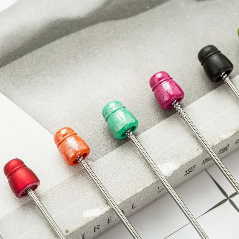 A collection of beadable ballpoint pens in various colors, including red, pink, and green, resting on a light surface.