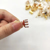 A hand holds a small, rose gold metal hair clip shaped like a butterfly wing.