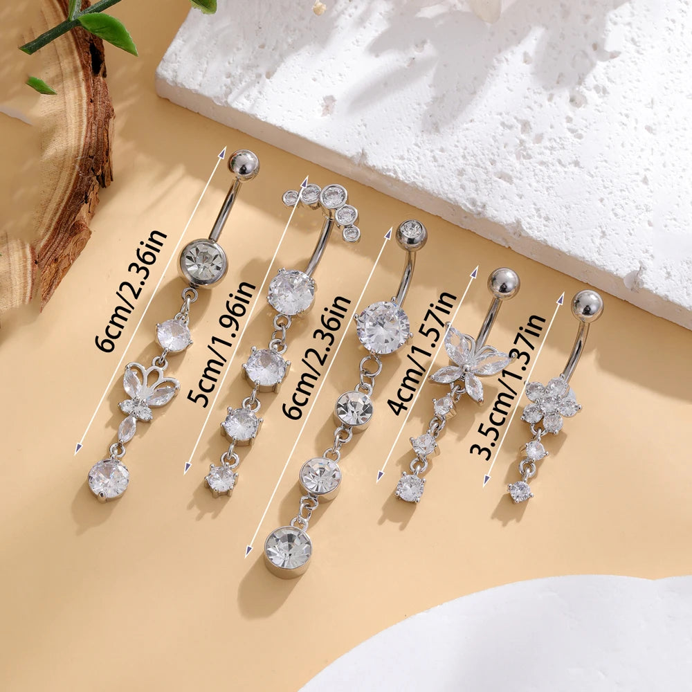 A set of five gold stainless steel dangled belly button rings with various chain lengths and floral charms displayed on a lig