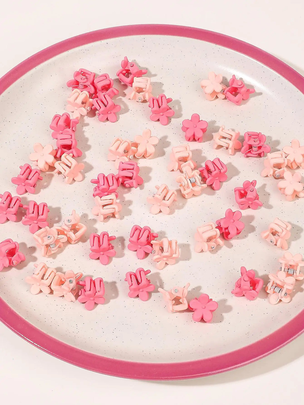 A collection of pink and coral mini flower hair clips arranged on a white plate.