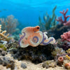 Une petite pince à cheveux en forme d'octopus orange translucide posée sur un fond de récif avec des plantes marines dans l'e