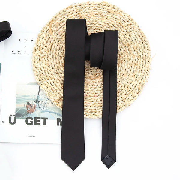 A black necktie is displayed on a woven straw mat next to a piece of paper.