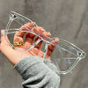Una mano sostiene unas gafas azules cuadradas y transparentes que bloquean la luz contra un fondo gris.