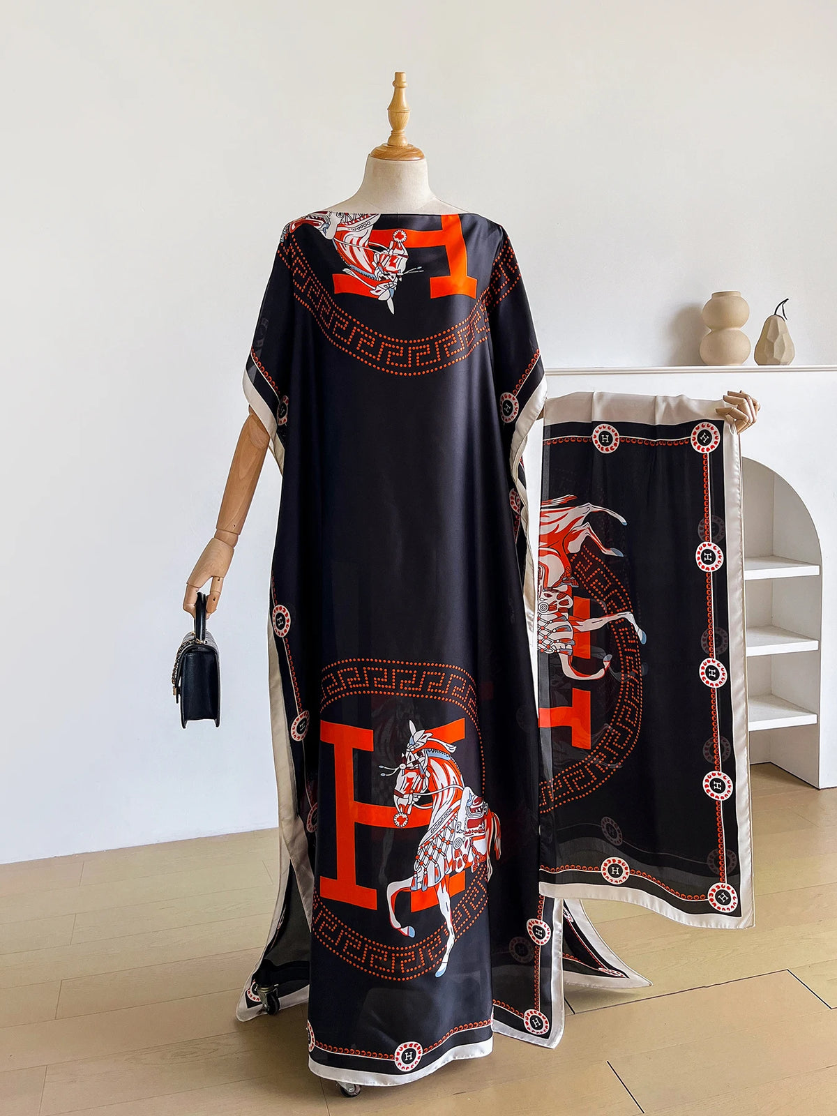 Abaya kaftan negra con estampado de caballo naranja y ribete dorado, exhibido en maniquí.