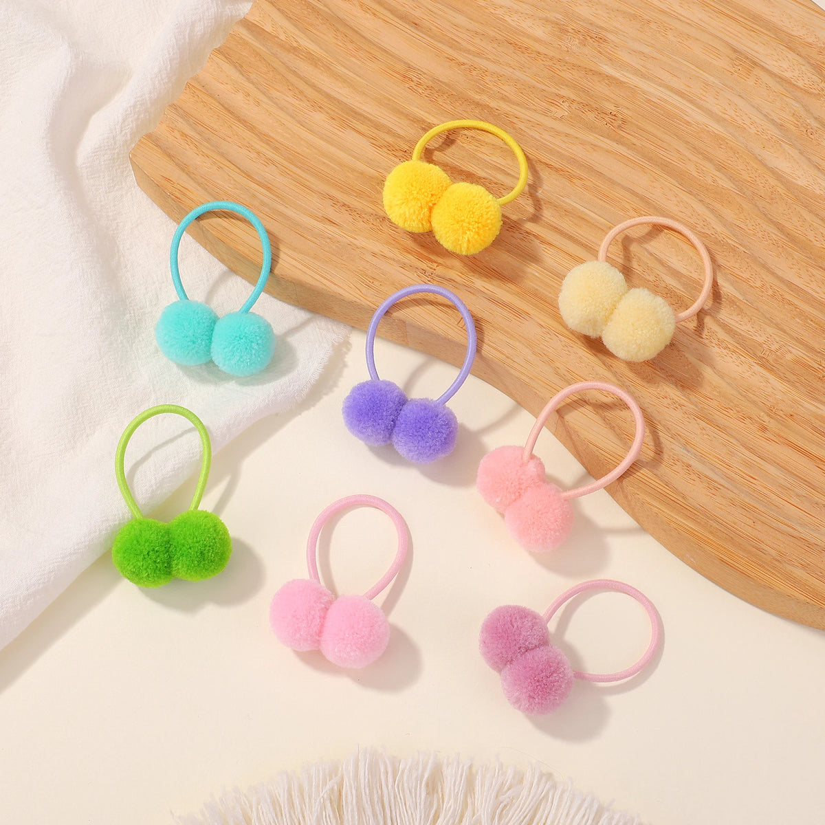 A collection of colorful double plush elastic hair bands in yellow, blue, purple, and pink resting on a wooden board.