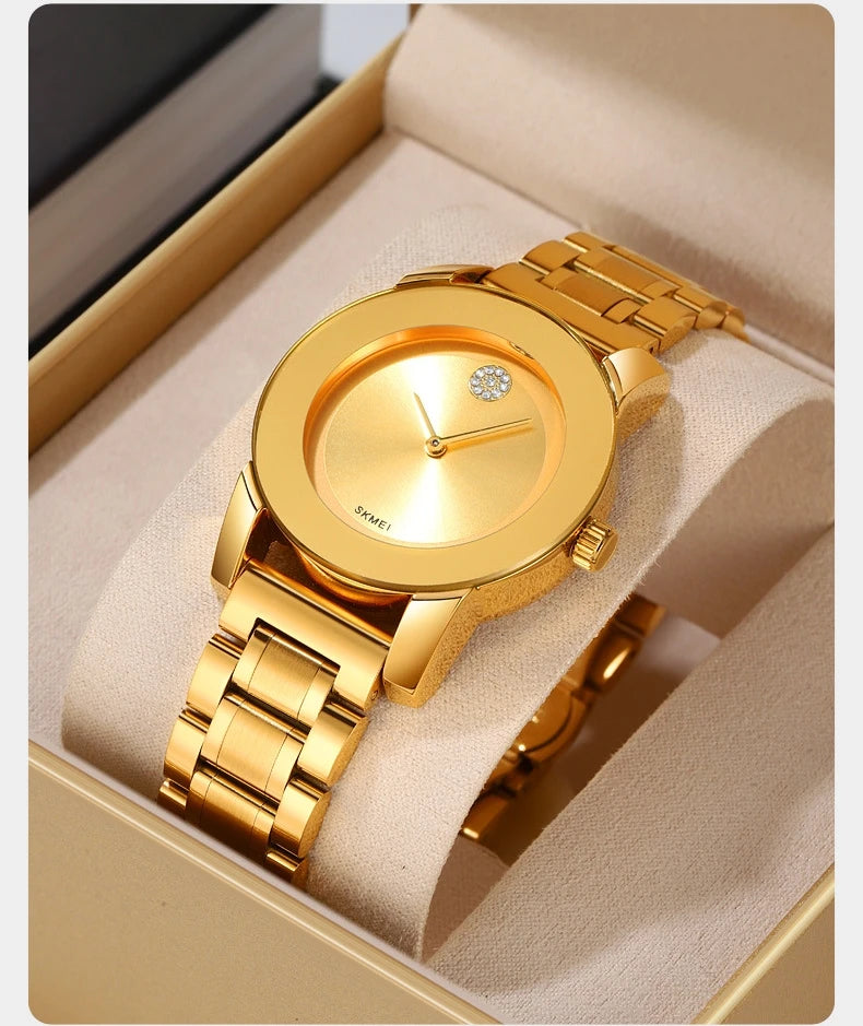 Reloj de cuarzo dorado con esfera redonda y pulsera de eslabones, exhibido dentro de una caja de color claro.