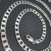 A silver geometric face chain necklace coiled on a dark background.