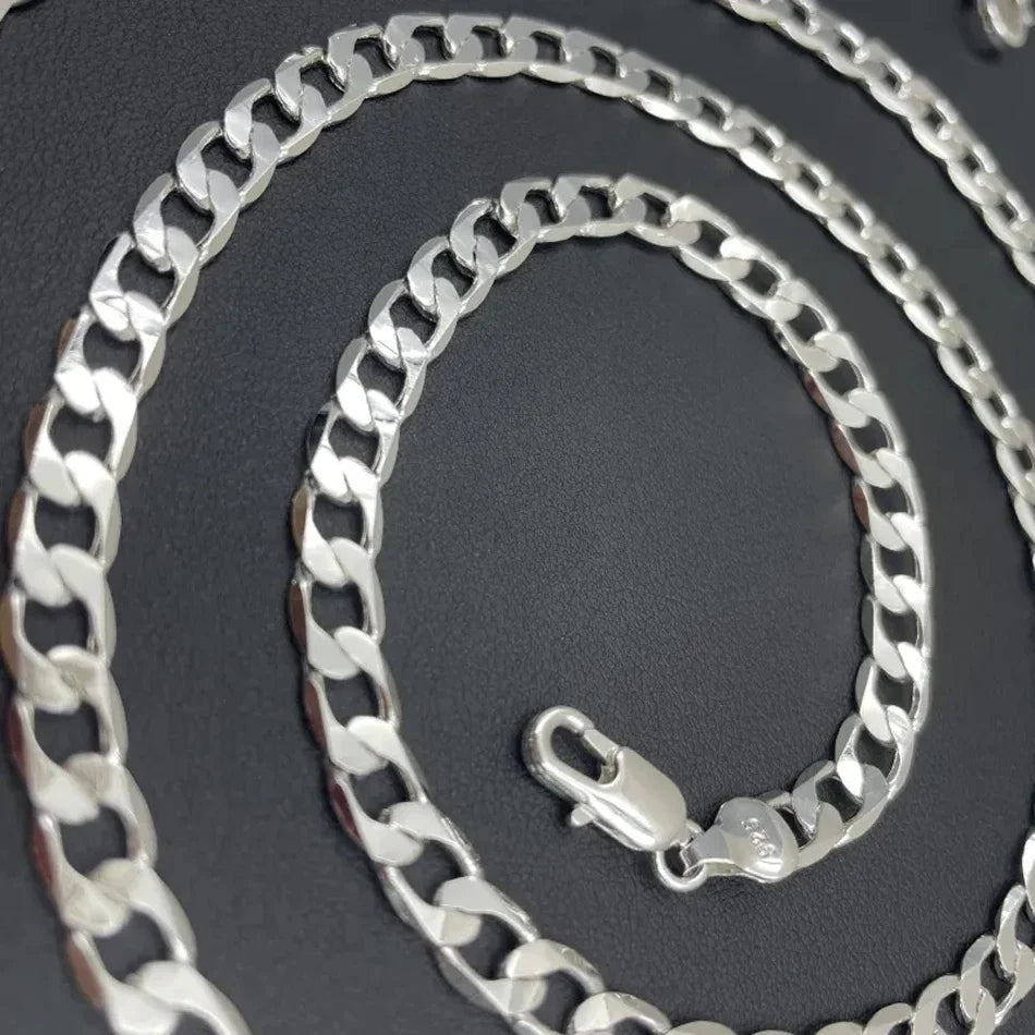A silver geometric face chain necklace coiled on a dark background.