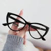 Eine Hand hält eine schwarze Vintage-Katzenauge-Lesebrille mit Goldakzenten vor weißem Hintergrund.