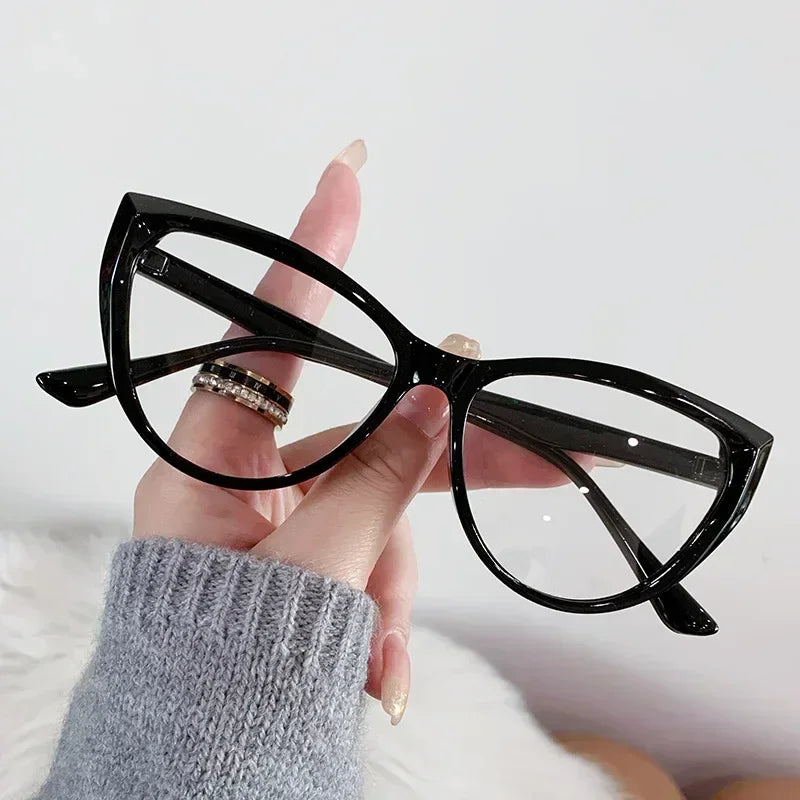 Eine Hand hält eine schwarze Vintage-Katzenauge-Lesebrille mit Goldakzenten vor weißem Hintergrund.