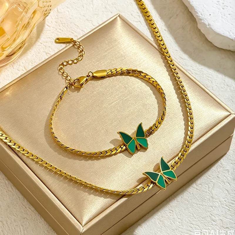 Ein Set aus goldfarbenen Schmetterlings-Anhänger-Halsketten und Armreifen, präsentiert in einer goldenen Box.
