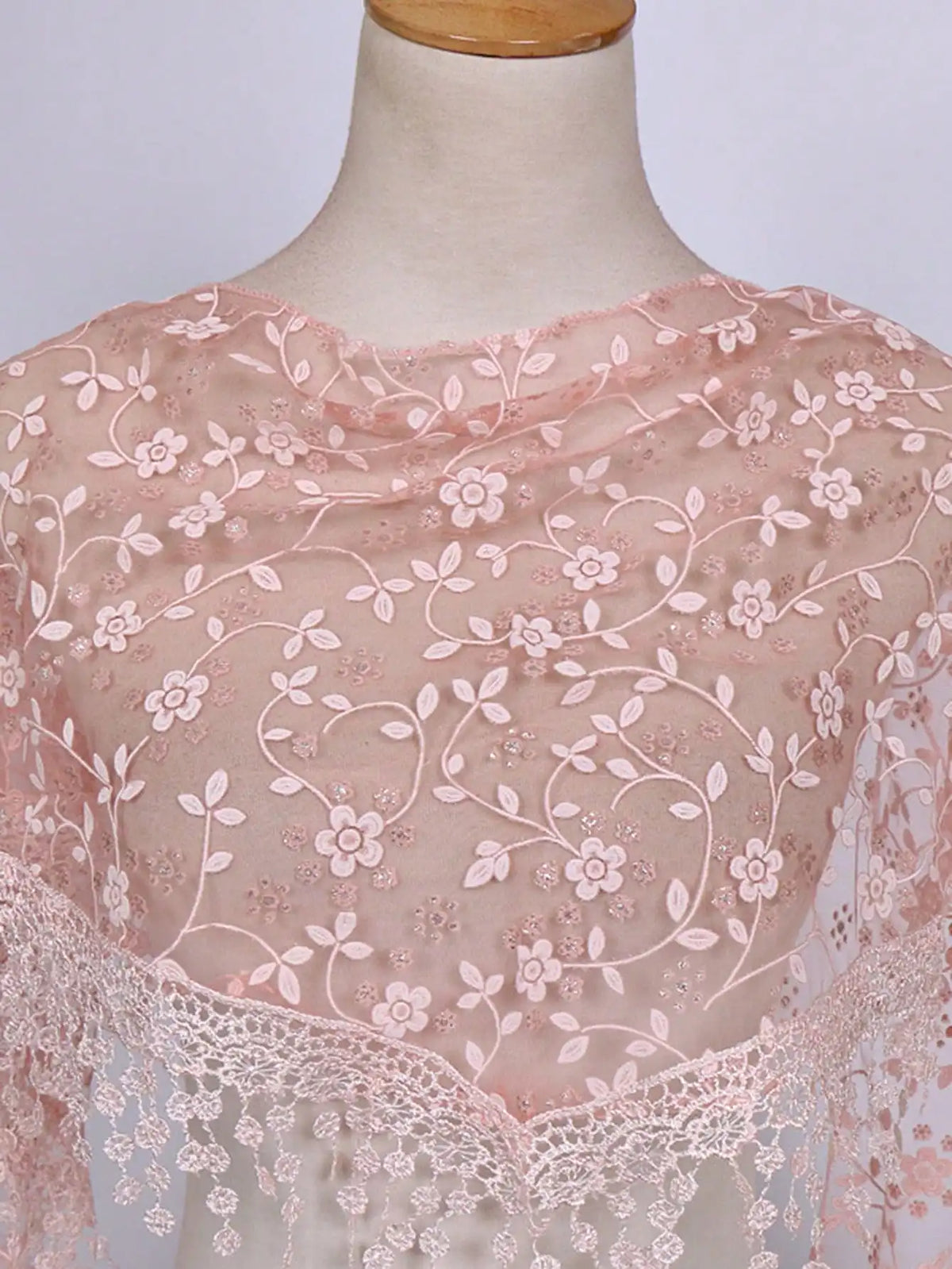 A sheer pink floral lace scarf draped over a mannequin's neck.