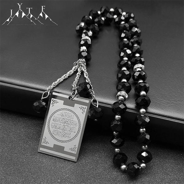 A black beaded necklace with a stainless steel Quran Arabic car pendant on a dark background.