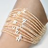 A stack of mother of pearl initial necklaces spelling out the letters T I S O N with crystal accents on a person's wrist.