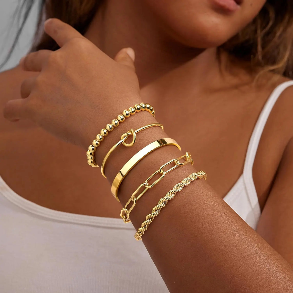 A close-up of a hand wearing several stacked 14K gold plated chunky cuff bangles on a wrist.