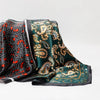 A luxurious satin silk scarf featuring intricate gold and green paisley patterns on a dark background.