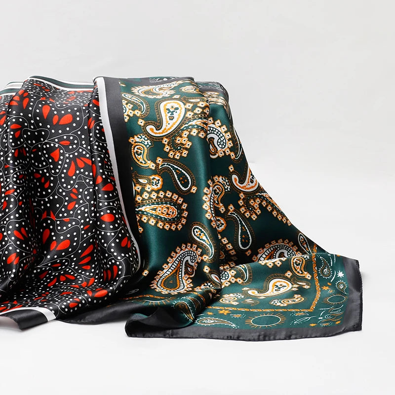 A luxurious satin silk scarf featuring intricate gold and green paisley patterns on a dark background.