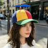 A woman wearing a funny multicolor propeller hat with blue, yellow, and red feathers on a city street.