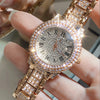 A close-up shot of a gold-toned wristwatch with a clear face and surrounding rhinestones being held by a person's fingers.