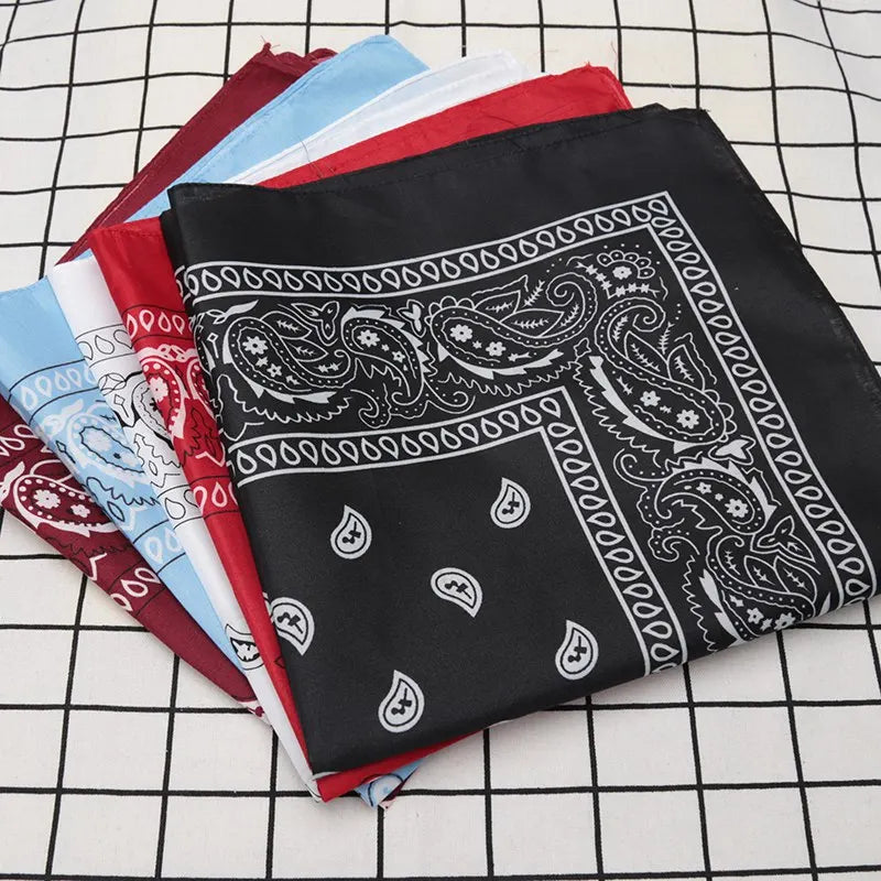 Una pila de pañuelos de tela de varios colores, incluyendo una bandana negra con patrones de paisley y florales blancos, colo